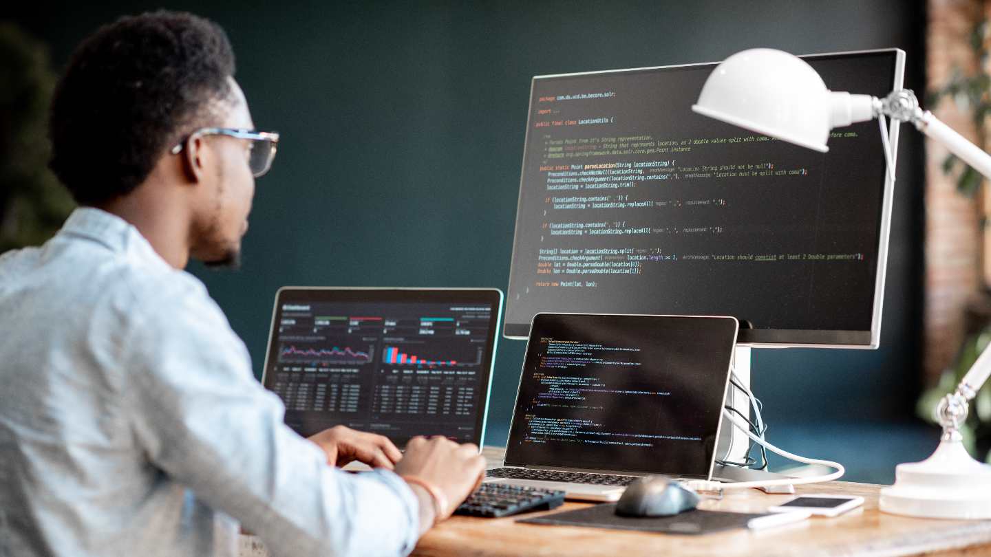 tech-pros-share-their-best-tips-for-writing-better-code Man sitting at desk with multiple monitors writing code.